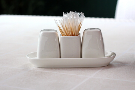 Close-up view of a set of cups for spices, salt, peppers and toothpicks, standing on a white table.の写真素材