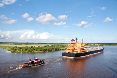 The movement of sea merchant ships and tugs to the entrance and exit from the port. View of the river Neches. Port Beaumont, Texas, USA. July 2017.の写真素材