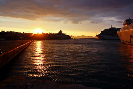 SHIPS AND FERRIES MOORED IN THE PORT AT SUNSET. CRUISE LINER DEPARTURE FROM THE HARBOR. PIRAEUS,...