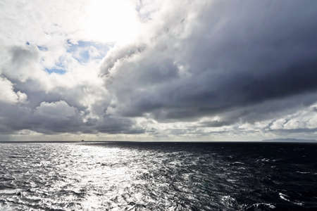 The clouds are multicolored, thunderous bizarre shapes against the blue sky and the sun above the...