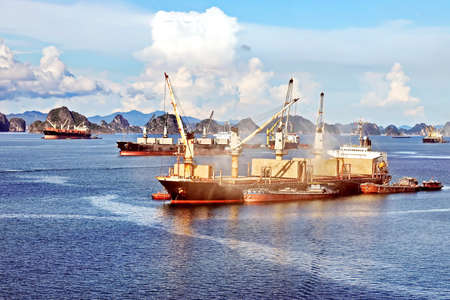 Seagoing vessels, barges, tugboats and small boats at the roadstead of Halong bay under cargo...
