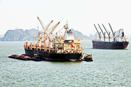 Seagoing vessels, barges, tugboats and small boats at the roadstead of Halong bay under cargo...