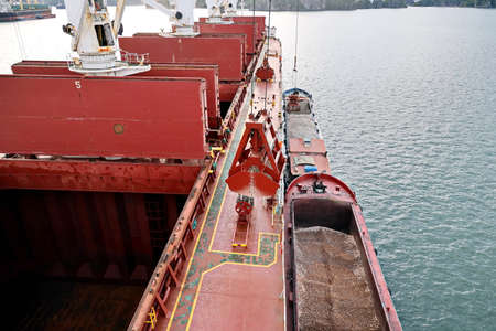 Loading bulk cargo of limestone from barges into a bulk carrier by using ship cranes and grabs at the port of Campha, Vietnam. October, 2020.の写真素材