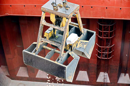 Loading bulk cargo of limestone from barges into a bulk carrier by using ship cranes and grabs at...