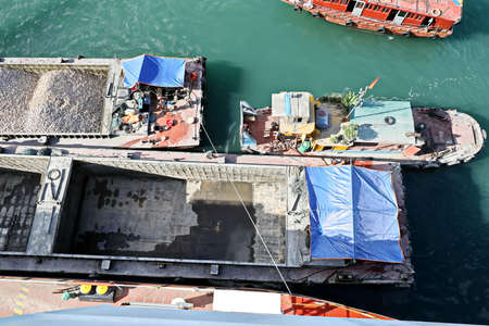 Loading bulk cargo of limestone from barges into a bulk carrier by using ship cranes and grabs at...