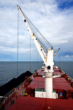 Loading coal from cargo barges onto a bulk carrier using ship cranes and grabs at the port of Muara...