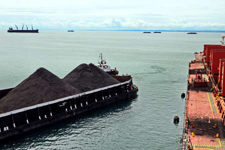 Loading coal from cargo barges onto a bulk carrier using ship cranes and grabs at the port of Muara Pantai, Indonesia., 2021.の写真素材