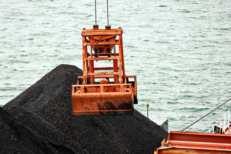 Loading coal from cargo barges onto a bulk carrier using ship cranes and grabs at the port of Muara...