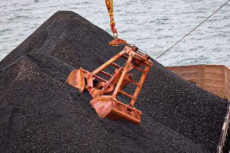 Loading coal from cargo barges onto a bulk carrier using ship cranes and grabs at the port of Muara Pantai, Indonesia. Close-up view of the work of bulldozers and loaders.の写真素材