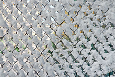 View of a frozen wire mesh fence covered with snow and ice on a bright sunny day. Background....