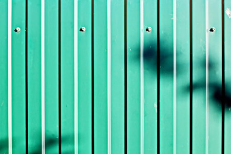 Green metal fence with shadow. Abstract background and texture for design.