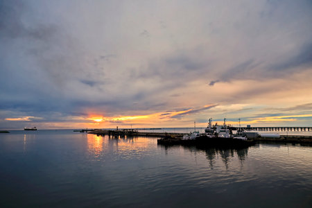 Sunset over the sea with fishing boats and pier in the foregroundの写真素材