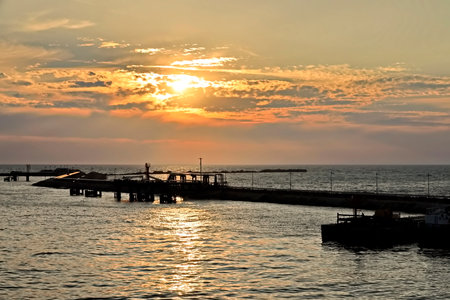 Sunset over the sea with a pier in the foreground and boats on the waterの写真素材