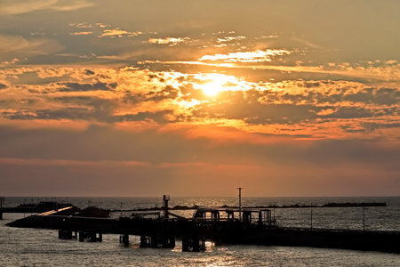Sunset over the sea with a pier in the foreground and the sky in the backgroundの写真素材