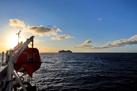 View of the sunset from the side of a ship with a red lifeboatの写真素材
