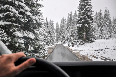 Man Driving in a Snow through mountain forest on winding roadの写真素材