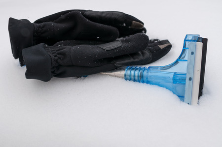 Closeup of snow and ice car cleaner with winter gloves on the snowの写真素材
