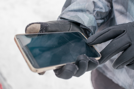 Closeup of man using smartphone in winter with winter gloves for touch screensの写真素材