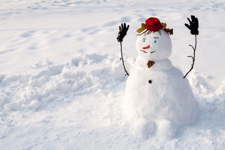 Smiling snowman with a mustache, woolen hat, gloves and carrot nose, outdoors in snowfallの写真素材