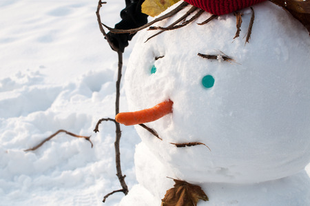 Closeup of smiling snowman with a mustache, woolen hat and carrot nose, outdoors in snowfallの写真素材
