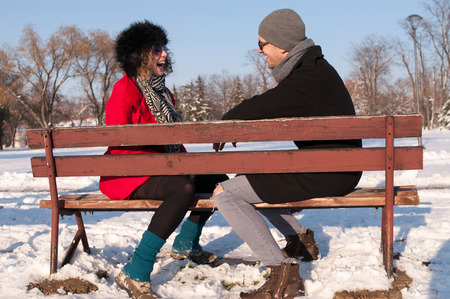 Young couple sitting on bench in park in winter and smilingの写真素材