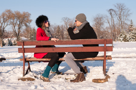 Young couple sitting on bench in park in winter and talkingの写真素材