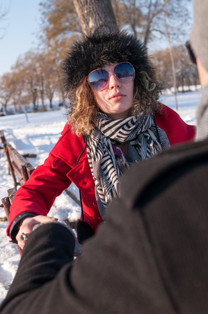 Young couple sitting on bench in park in winter and talkingの写真素材