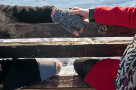 Young couple holding hands on bench in park in winterの写真素材