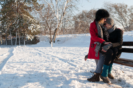 Young couple sitting on bench in park in winter and smilingの写真素材