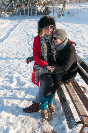 Young couple in love sitting on a bench in a park in Winter and smilingの写真素材