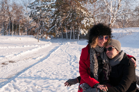Young couple in love sitting on a bench in a park in Winter and smilingの写真素材