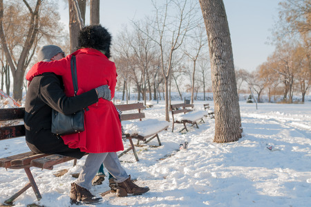 Young couple sitting on bench in park in winterの写真素材