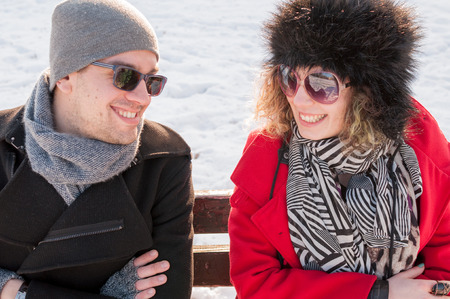 Young couple sitting on bench in park in winter and smilingの写真素材