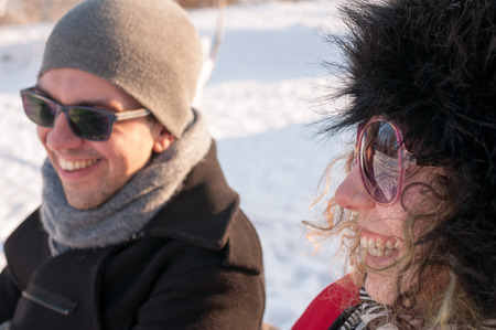 Young couple sitting on bench in park in winter and smilingの写真素材