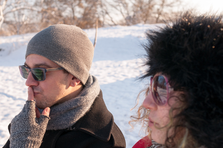 Young couple sitting on bench in park in winter and thinkingの写真素材