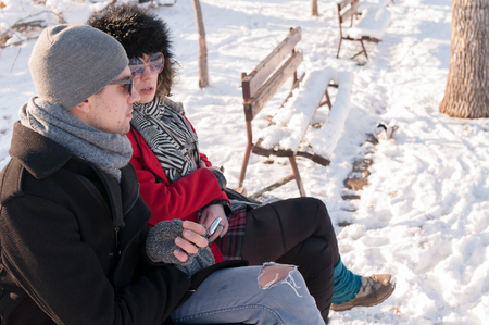 Young couple sitting on bench in park in winter and talkingの写真素材