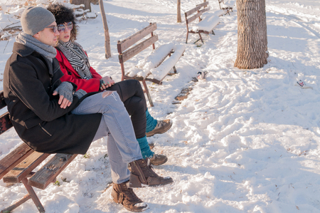 Young couple sitting on bench in park in winter and talkingの写真素材