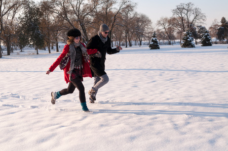 Couple walking and running in winter forest happy and joyful holding hands on romantic date in winter snow forest landscape.の写真素材