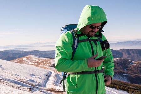 Hiker checking his smartphone on the top of the mountainの写真素材