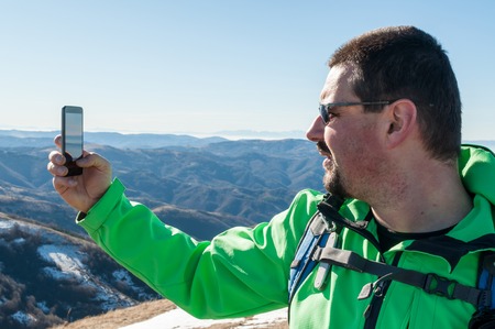Young backpacking man taking a photo of himself in mountains with smart phoneの写真素材