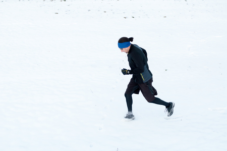 Healthy young man jogging outside on snow, athlete running on winter dayの写真素材