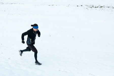 Healthy young man jogging outside on snow, athlete running on winter dayの写真素材