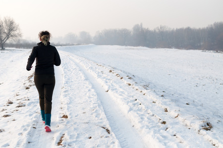 Healthy young woman jogging outside on snow, athlete running on beautiful winter dayの写真素材