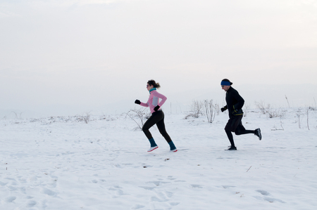 Healthy young couple jogging outside on snow, athlete running on winter dayの写真素材