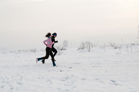 Healthy young couple jogging outside on snow, athlete running on winter dayの写真素材