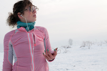 Girl runner enjoying outside on snow after running on winter day and listen music in earphones from smartphone.の写真素材