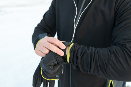 Runner using heart rate monitor, smartwatch checking performance or GPS. Man athlete looking at stopwatch. Technology for tracking activity. Outside, snow, winterの写真素材