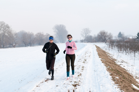 Healthy young couple jogging outside on snow, athlete running on beautiful winter dayの写真素材