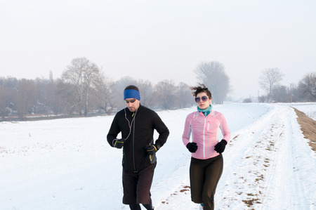 Healthy young couple jogging outside on snow, athlete running on beautiful winter dayの写真素材