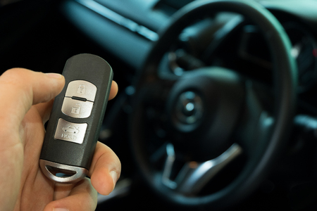 hand holding black wireless key car with background steering wheel car interiorの写真素材